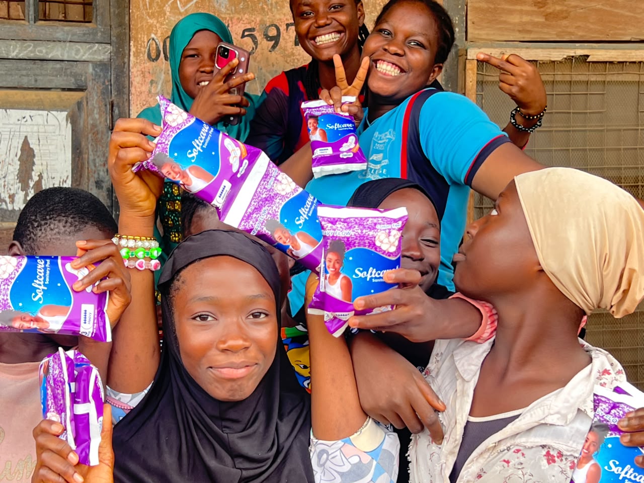 Girls and an outreach volunteer holding packs of sanitary pads in Ibadan